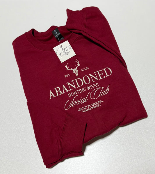 Red embroidered sweatshirt with Abandoned Hunting Wives Social Club design